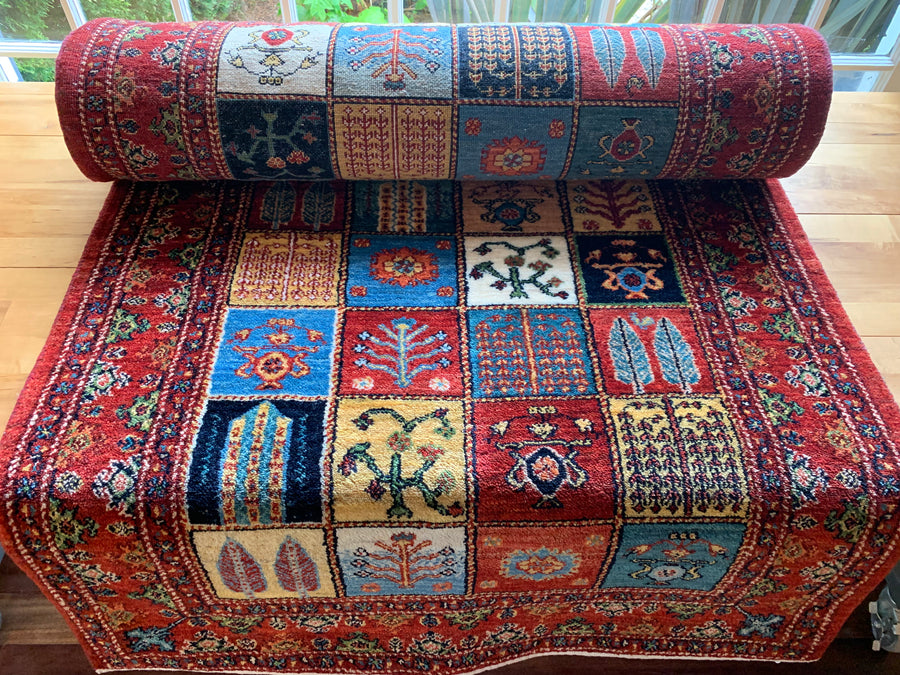 Classic traditional Persian carpet runner with squares of trees and plants framed by a red border with blue flowers.