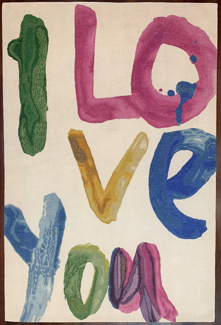 A wool 6x9 area rug with the words I Love You hand-knotted as a blend of wool and silk in bright green, pink, yellow, and blue against a neutral toned wool pile background. 