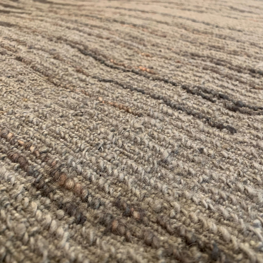 Close-up detail of The Stelig handmade rug from Battilossi in Baraf color-way. The flatwoven texture is in browns, grey, and beige tones. 
